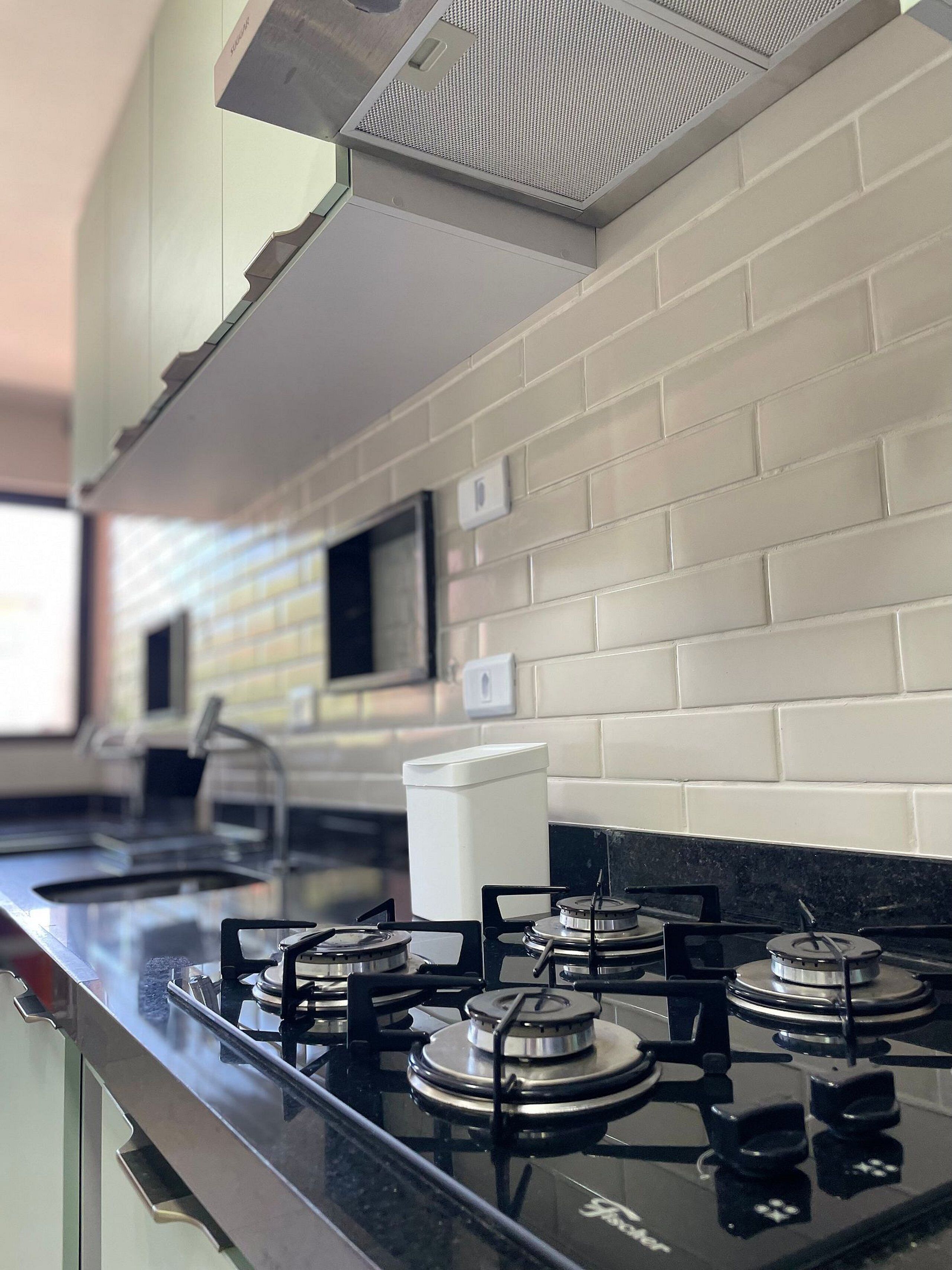 Une cuisine moderne dotée d’une cuisinière à gaz, de carreaux de céramique blancs disposés en motif métro et d’un dosseret en acier inoxydable.