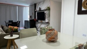 A modern living room with a dining table, sofa, and a TV in the background. - Flat 2 quartos no Dubourcq Residence  (Ipojuca)