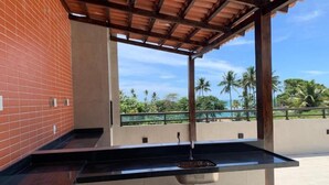 An outdoor kitchen area with a sink and a view of palm trees and greenery. - Flat 2 quartos no Dubourcq Residence  (Ipojuca)
