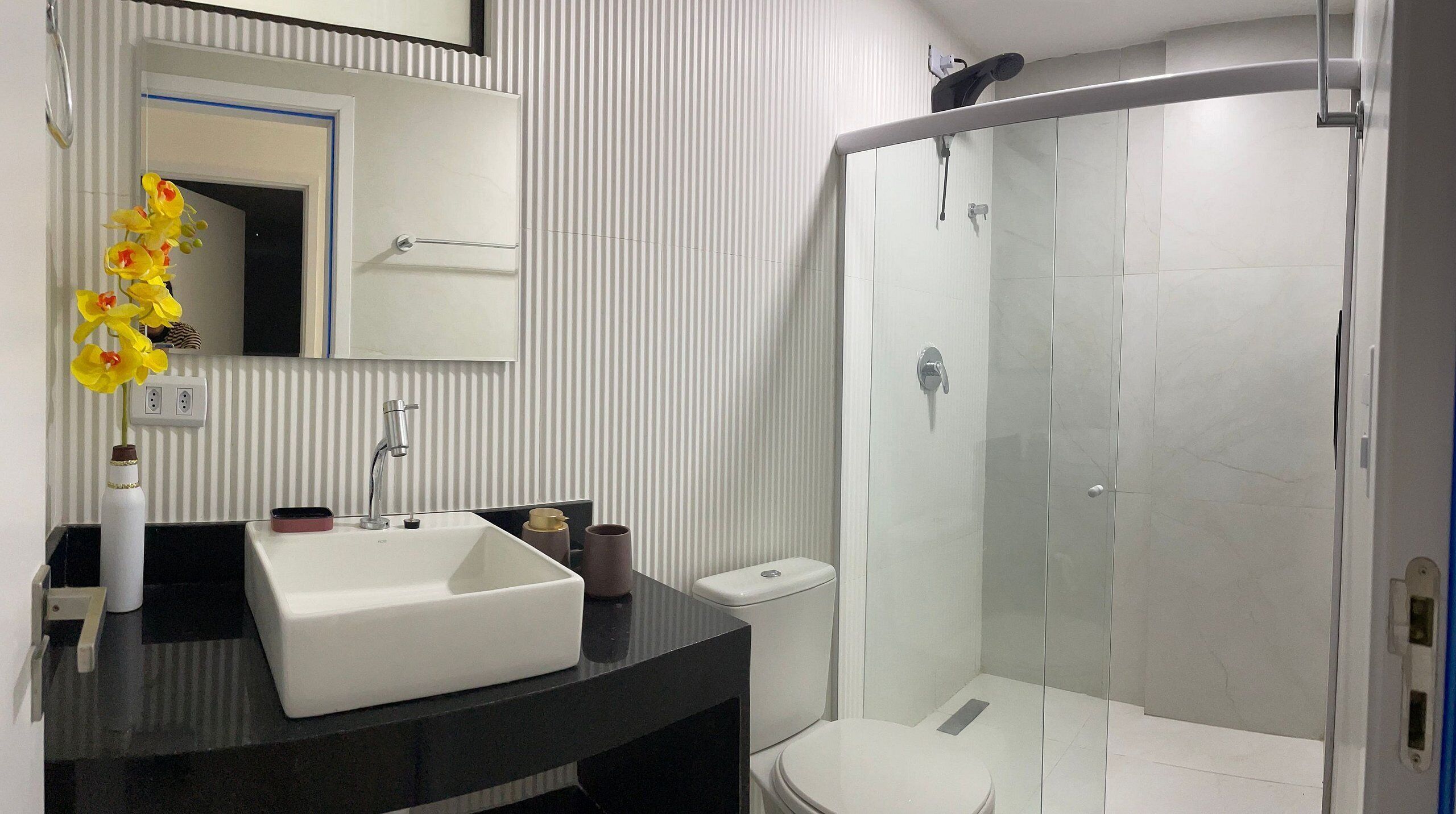 Ein modernes Badezimmer mit einem weißen Waschbecken, einem Spiegel darüber, einer Toilette und einer Duschkabine aus Glas.