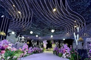 Un espacio interior con un sendero bordeado por arreglos florales y un techo decorado con luces colgantes.