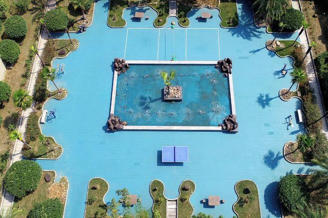 Ein Luftbild eines Schwimmbeckens mit einer zentralen Insel, umgeben von Palmen und Liegestühlen.