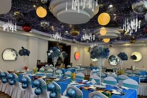Un salón de banquetes con mesas dispuestas para un evento formal, con iluminación decorativa colgante y decoración temática celestial.