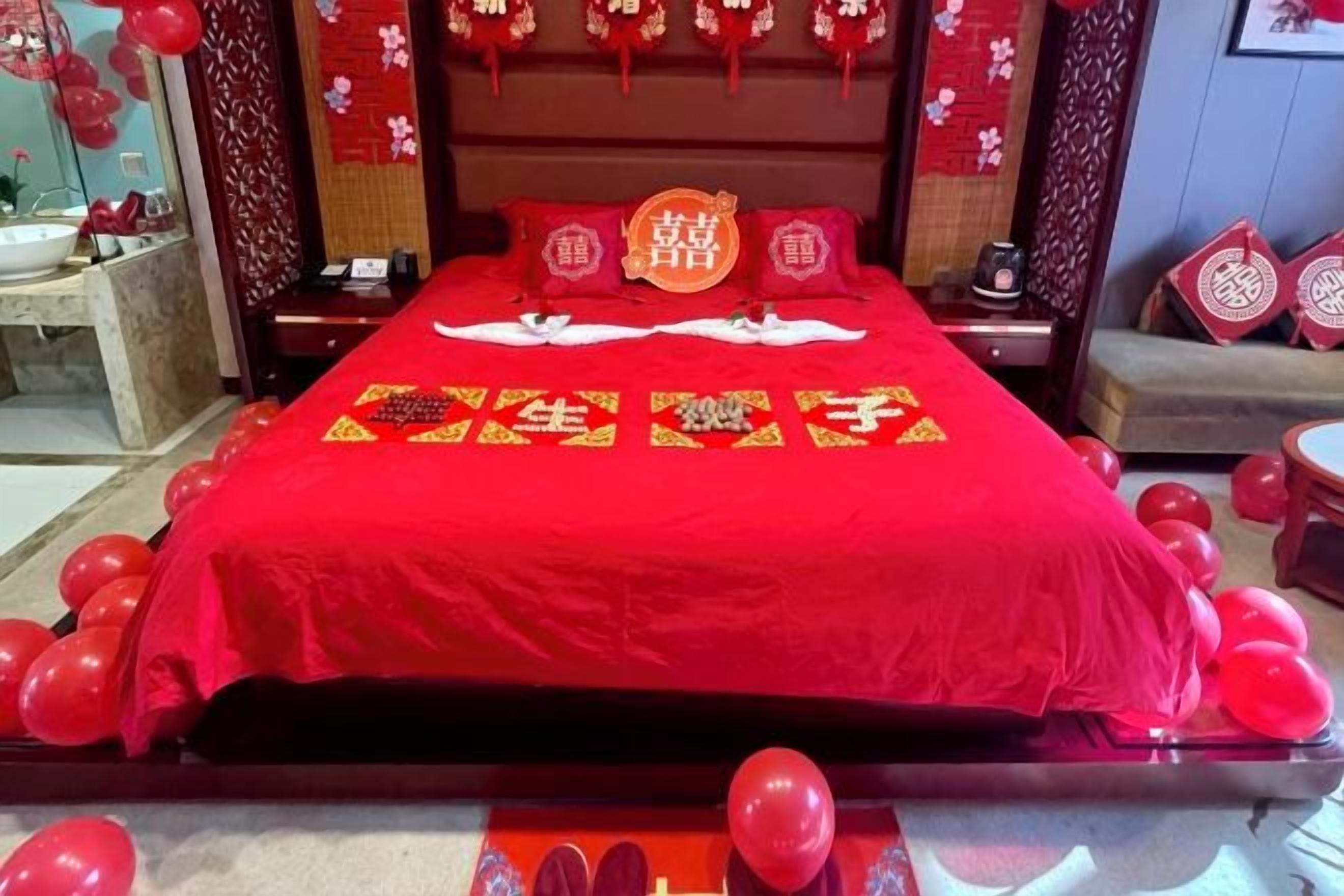 Un lit avec une couverture rouge et des oreillers, entouré de ballons rouges.
