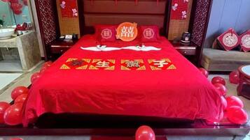 A bed with a red bedspread and pillows, surrounded by red balloons.