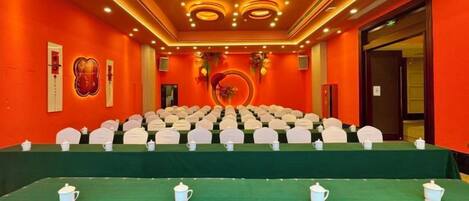 A conference room with a green carpet, white chairs, and a table with teapots.