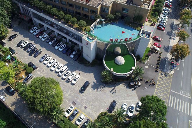 Vista aérea de un hotel con piscina, estacionamiento y un área ajardinada con una escultura esférica.