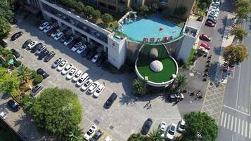 Vista aérea de un hotel con piscina, estacionamiento y un área ajardinada con una escultura esférica.
