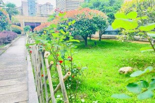 Un sendero atraviesa un jardín con cerdaña de madera, césped verde y árboles con flores rojas.