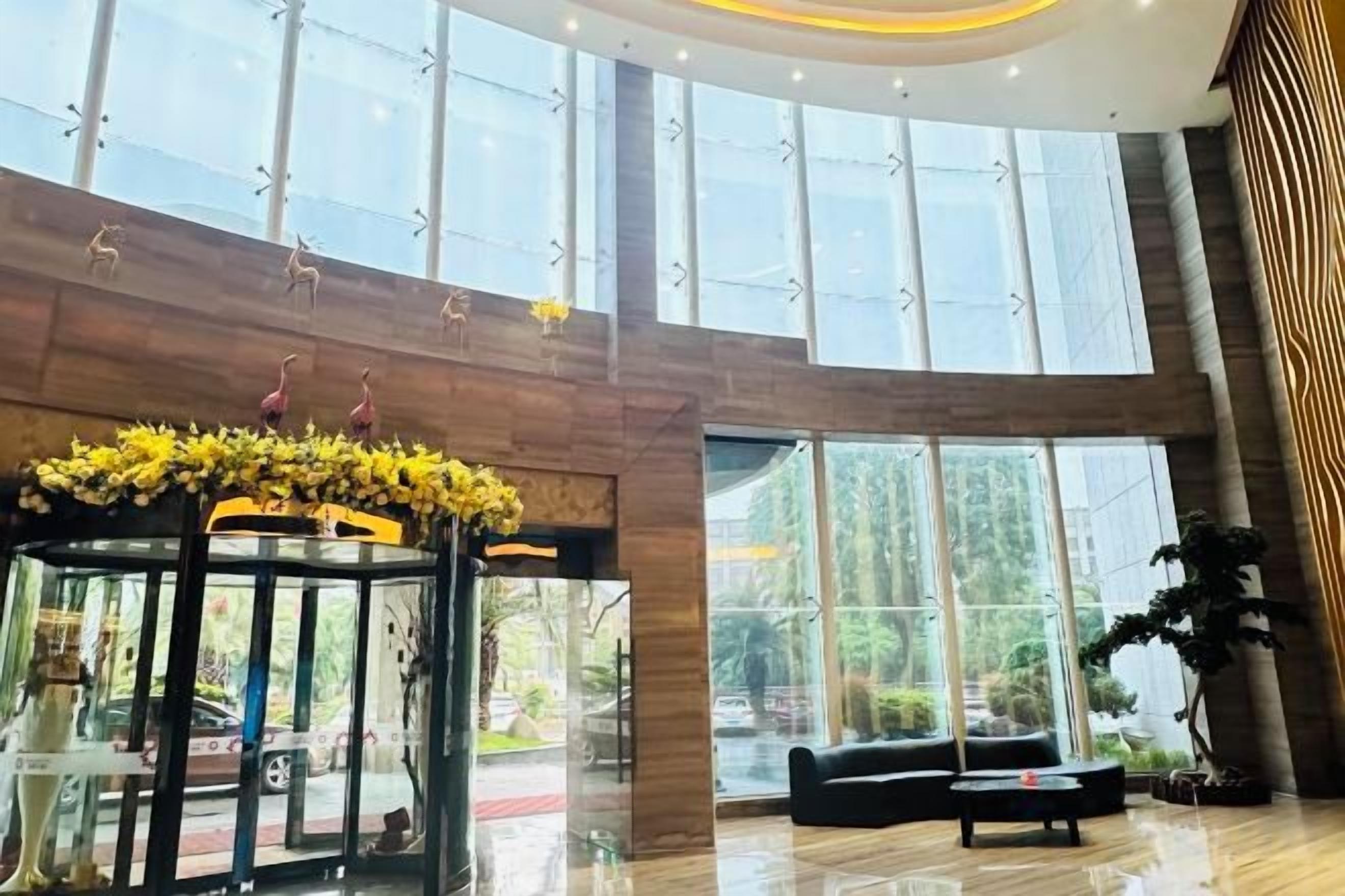 Um hall amplo com teto de vidro, área de estar central e arranjo floral decorativo.