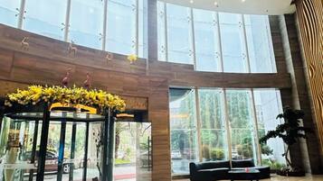 Um hall amplo com teto de vidro, área de estar central e arranjo floral decorativo.