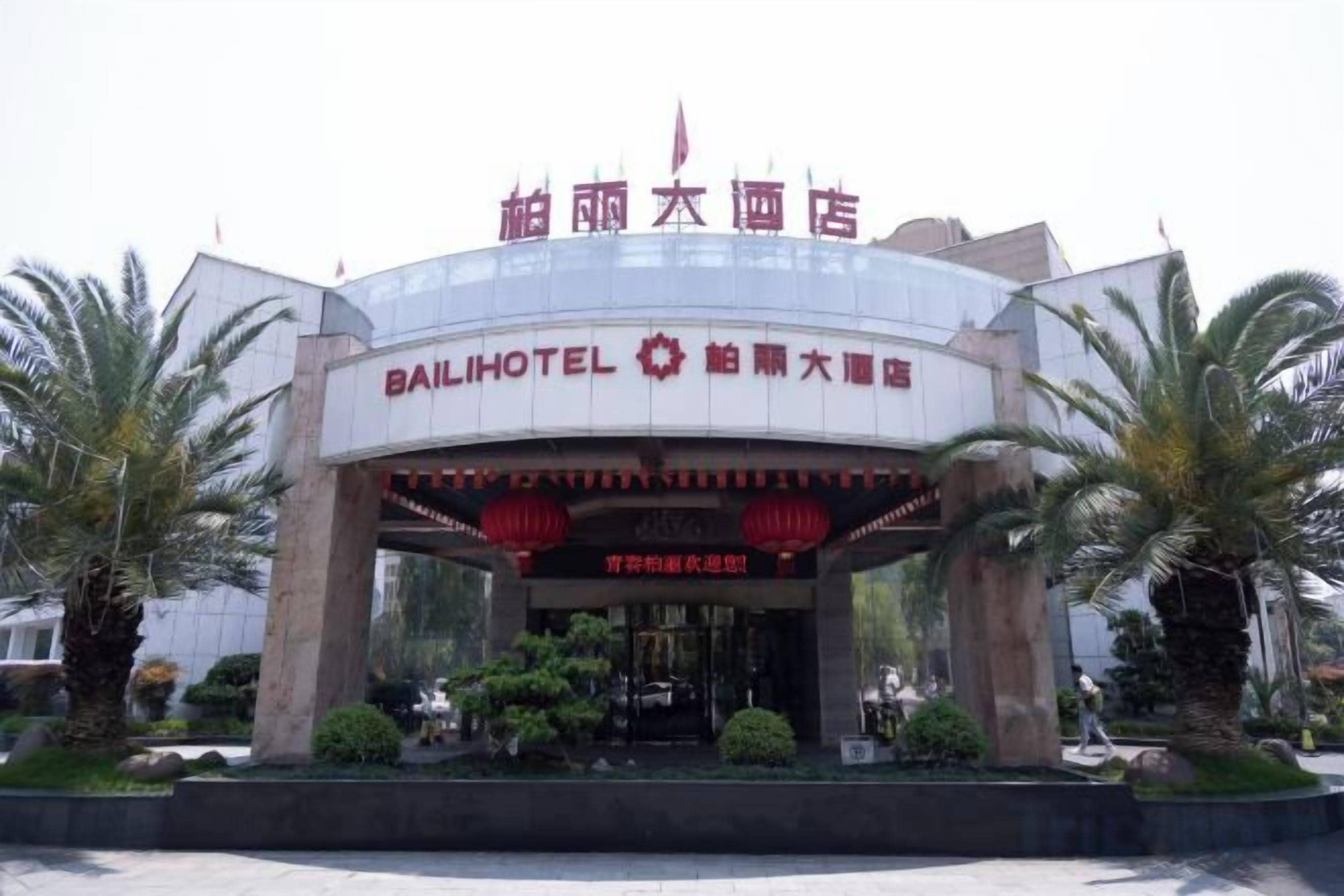 L’entrée d’un hôtel, avec une enseigne bien visible, un drapeau rouge et des palmiers.