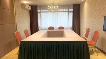A conference room with a long table, red chairs, a chandelier, and a large window with curtains.