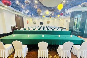 Un salón de conferencias con una larga mesa, sillas blancas y un mantel verde.