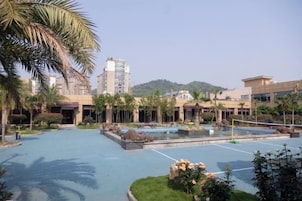 Un patio de hotel con piscina, palmeras y vistas a una colina.