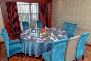 Una mesa de comedor redonda con sillas tapizadas en azul, dispuesta para una comida con platos, vasos y un centro de mesa.