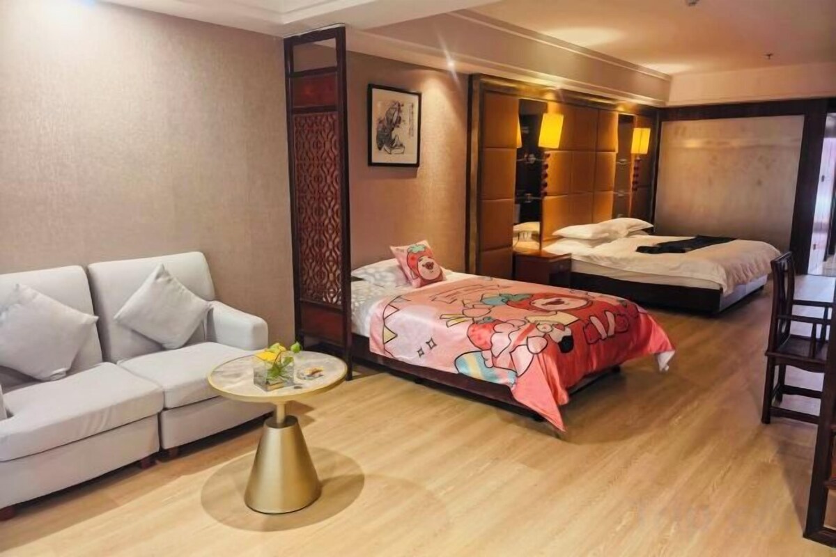 Une chambre d’hôtel avec un canapé, un lit recouvert d’une courtepointe aux couleurs vives, une petite table ronde ornée d’un vase et un plancher en bois.