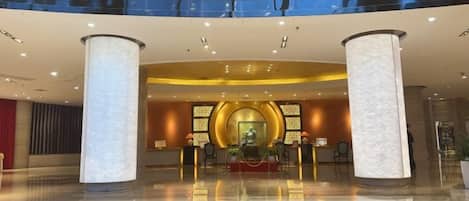 A hotel lobby with a circular reception desk, two large pillars, and a polished floor.