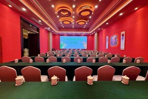 Un salón de conferencias con filas de mesas y sillas, una pantalla grande al frente y paredes rojas.