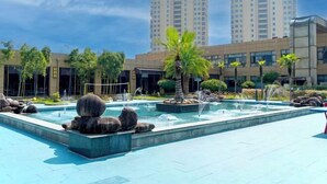 A modern outdoor pool area with water features, palm trees, and a backdrop of high-rise buildings. - Baili Hotel (Changshan)