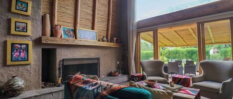 Una sala de estar acogedora con chimenea, asientos cómodos y grandes ventanales que ofrecen vistas al exterior.