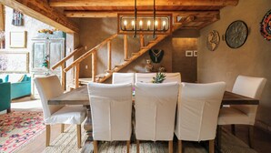 A dining area with a wooden table and white chairs, a staircase, and a chandelier. - Mayupata in Calca by Wynwood House (Calca)