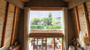 A room with a large window, wooden beams, and a view of greenery and buildings outside. - Mayupata in Calca by Wynwood House (Calca)