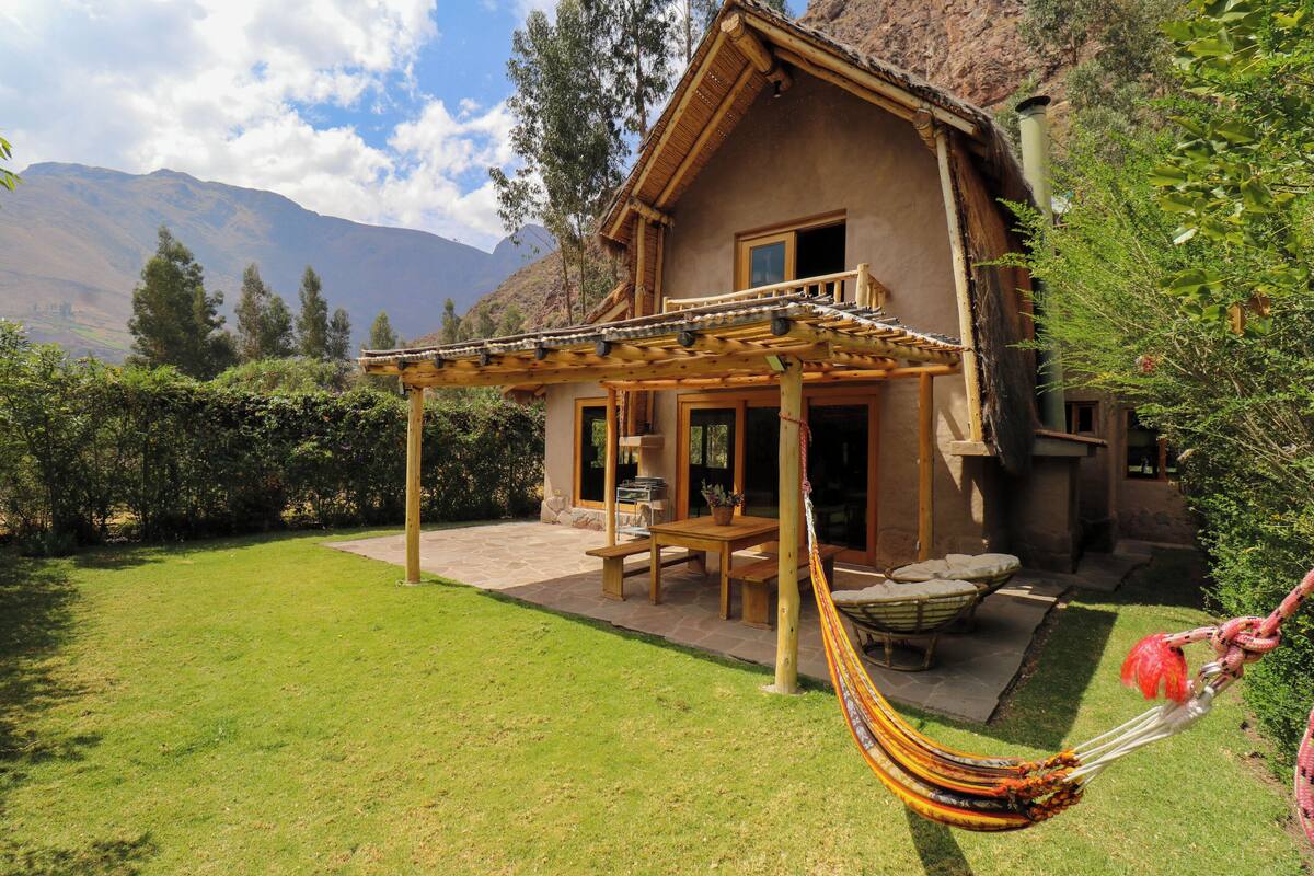 A wooden house with a patio, a hammock, and a mountain backdrop.