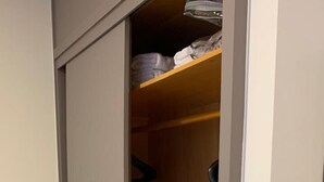Un dormitorio con armario correderas, una cama con ropa de cama blanca y un aparador de madera.