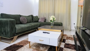Un soggiorno con un divano verde, un tavolino da caffè bianco con un telecomando e una TV su un mobile.