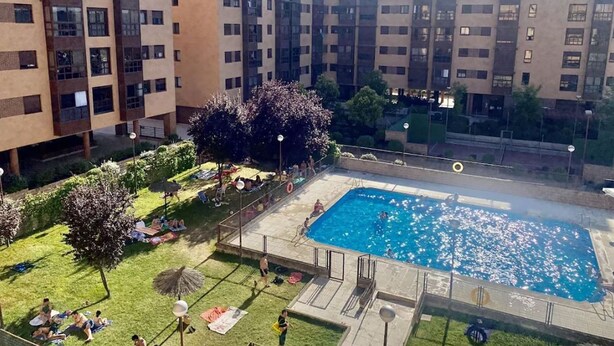 A residential building with a rooftop swimming pool surrounded by greenery and trees.