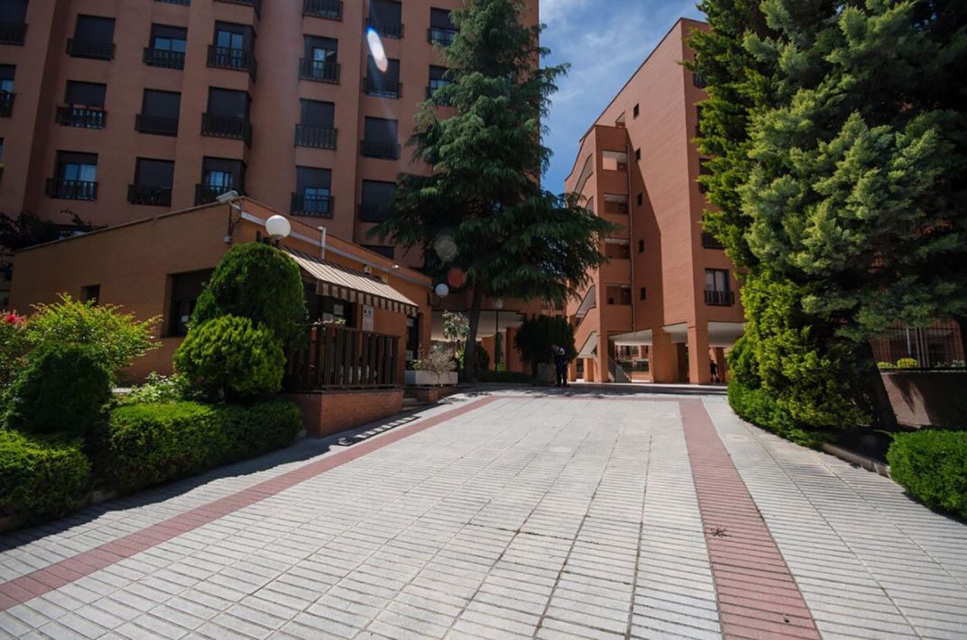 Une cour avec un chemin pavé, entourée de bâtiments dotés de balcons et d’une petite construction couverte.