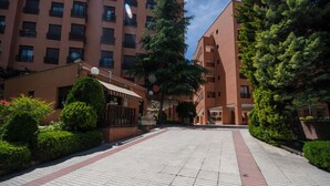 A courtyard with a paved walkway, surrounded by buildings with balconies and a small structure with a roof.