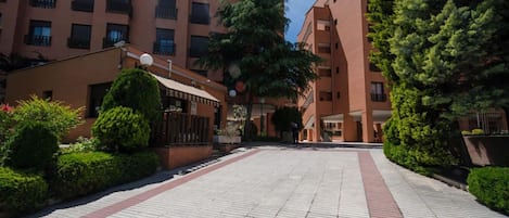 Un patio con un camino empedrado, rodeado de edificios con balcones y una pequeña estructura con techo.