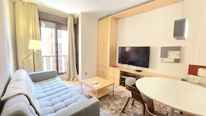 A modern hotel room with a sofa, a small table, a TV, and a dining area.