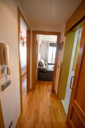 A narrow hallway with wooden flooring leading to a room with a bed and a window. - campezo (Madrid)
