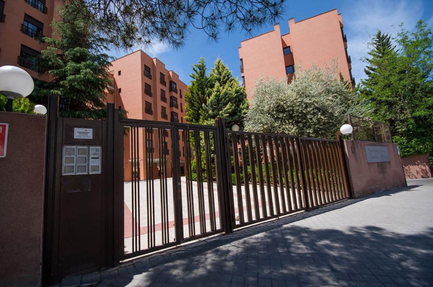 Una entrada vigilada a un edificio de varios pisos, rodeado de árboles y un cielo despejado.