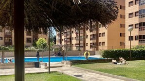 A residential building with a swimming pool, a covered patio area, and a grassy lawn.