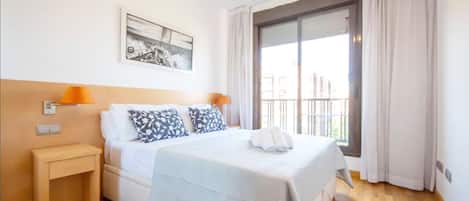 A hotel room with a bed, a nightstand, a lamp, a painting on the wall, and a window with curtains.