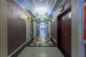 Un couloir d’hôtel avec un sol à carreaux, des portes de chaque côté et un lustre.