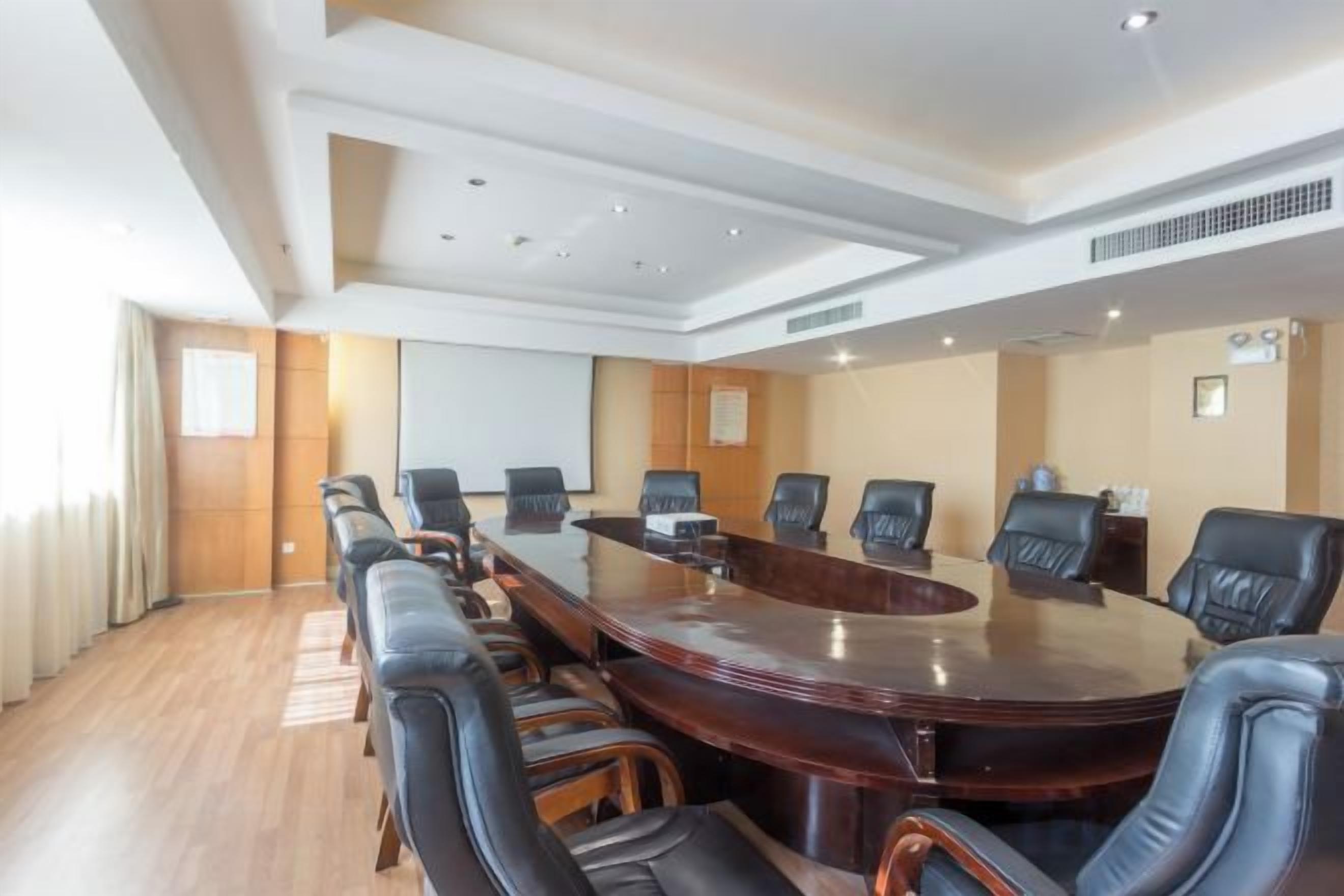 A conference room with a large oval table, black leather chairs, and a projector screen.