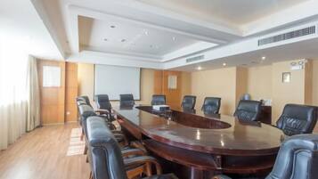 A conference room with a large oval table, black leather chairs, and a projector screen.