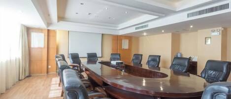 A conference room with a large oval table, black leather chairs, and a projector screen.