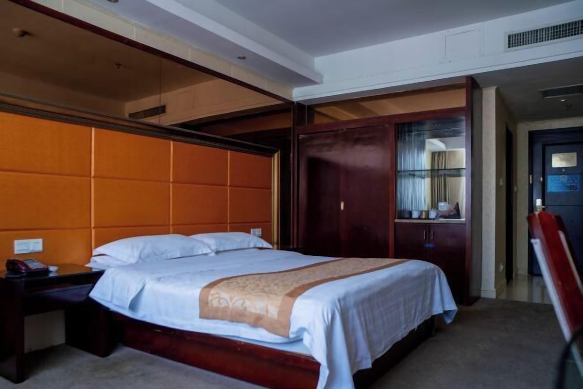 Ein Hotelzimmer mit einem großen Bett, einem Holzkopfstück, einem Nachttisch und einem Kleiderschrank.