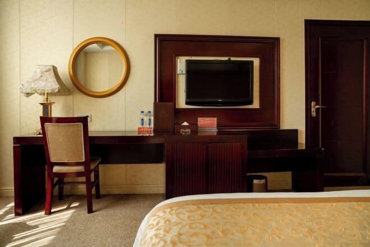 Ein Hotelzimmer mit einem Bett, einem Schreibtisch mit Stuhl, einem Fernseher, einem Spiegel und einer Tür.