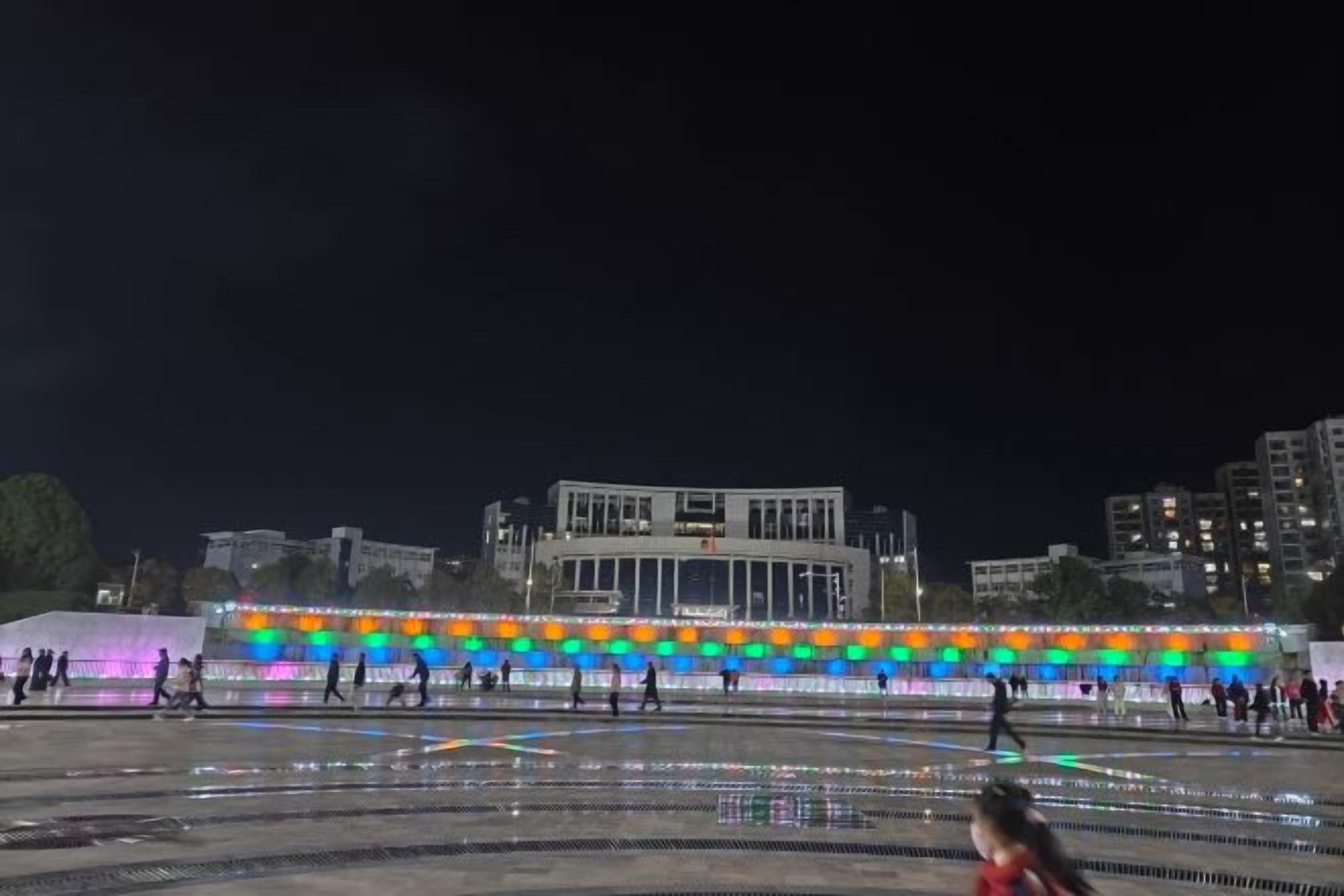 A nighttime view of a plaza with a brightly lit building in the background.