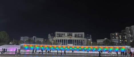 A nighttime view of a plaza with a brightly lit building in the background.