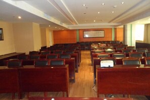A conference room with rows of chairs and tables, a projector screen, and a wooden panel wall. - Junhao Hotel (Xiushui)