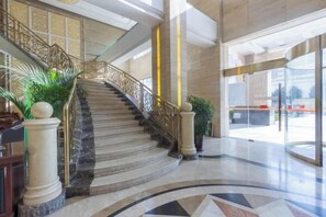 A grand staircase with marble steps and golden railings, leading to a modern lobby with a curved floor design and large glass doors. - Junhao Hotel (Xiushui)