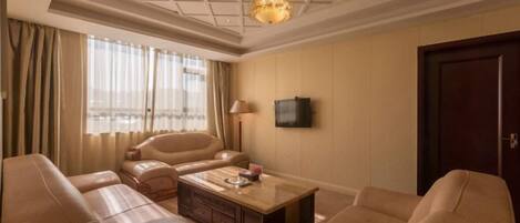 Habitación de hotel con un ventanal grande, un televisor de pantalla plana, una mesa de centro de madera y sofás de cuero color beige.